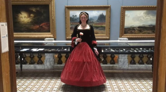 En kvinna står i renässanskläder och håller i en blomma.