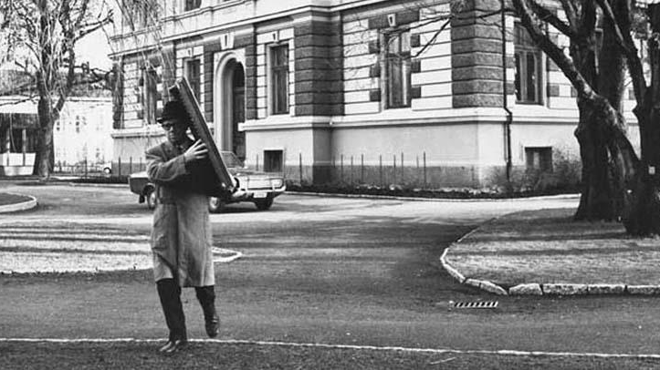 En man bär en tavla . Mannen är klädd i en vaktmästarrock och hatt.