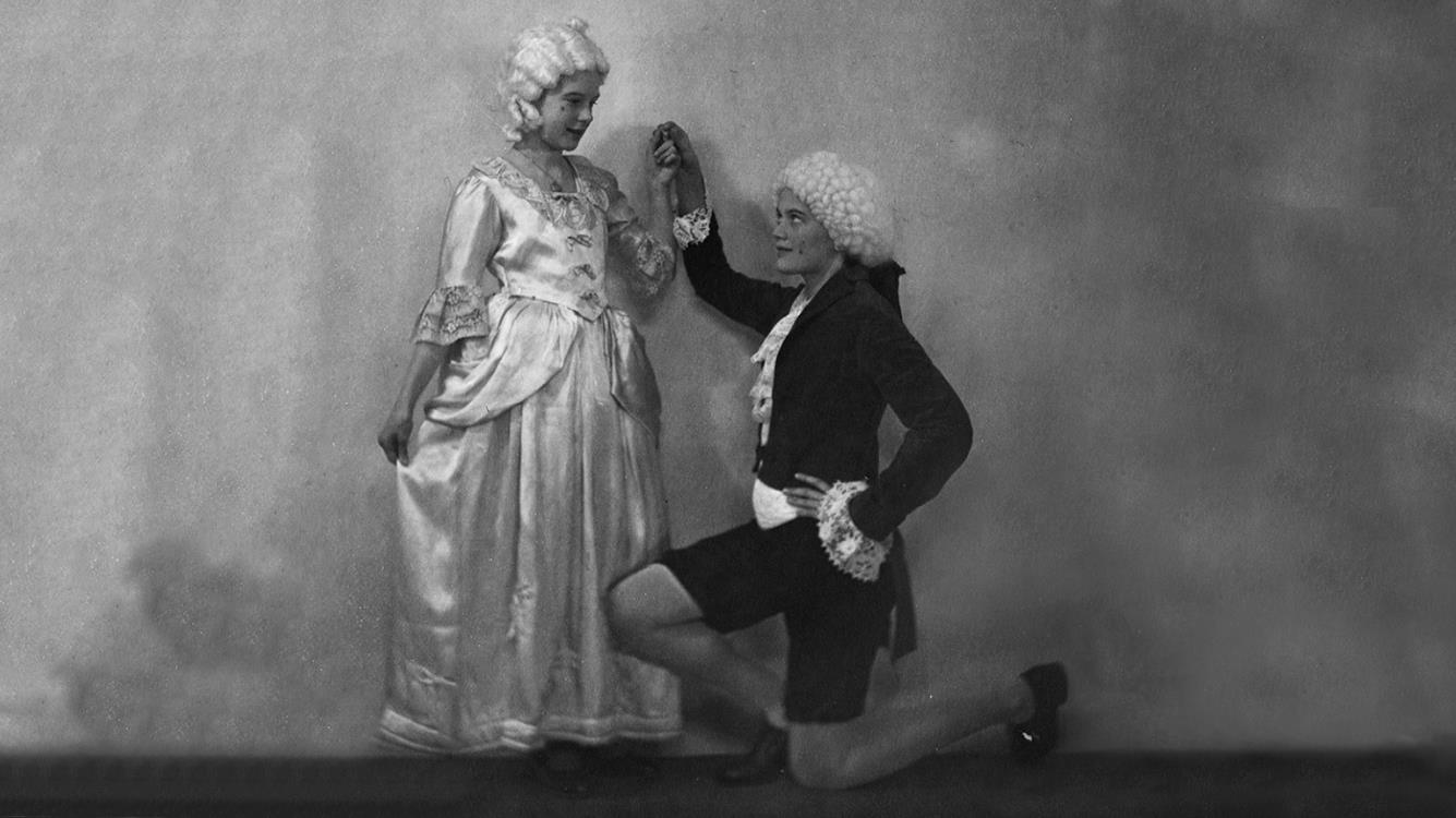 Ett barn knäfaller inför ett annat barn. Barnen är klädda i 1700-talskläder