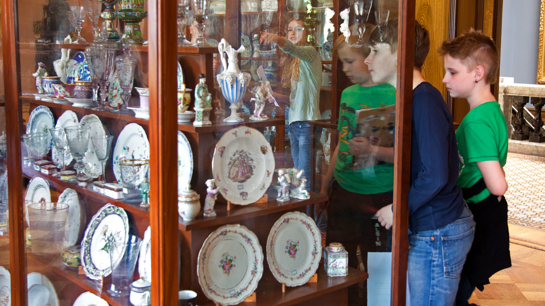 Tre barn tittar in i en äldre glasmonter med porslin- och glasföremål.