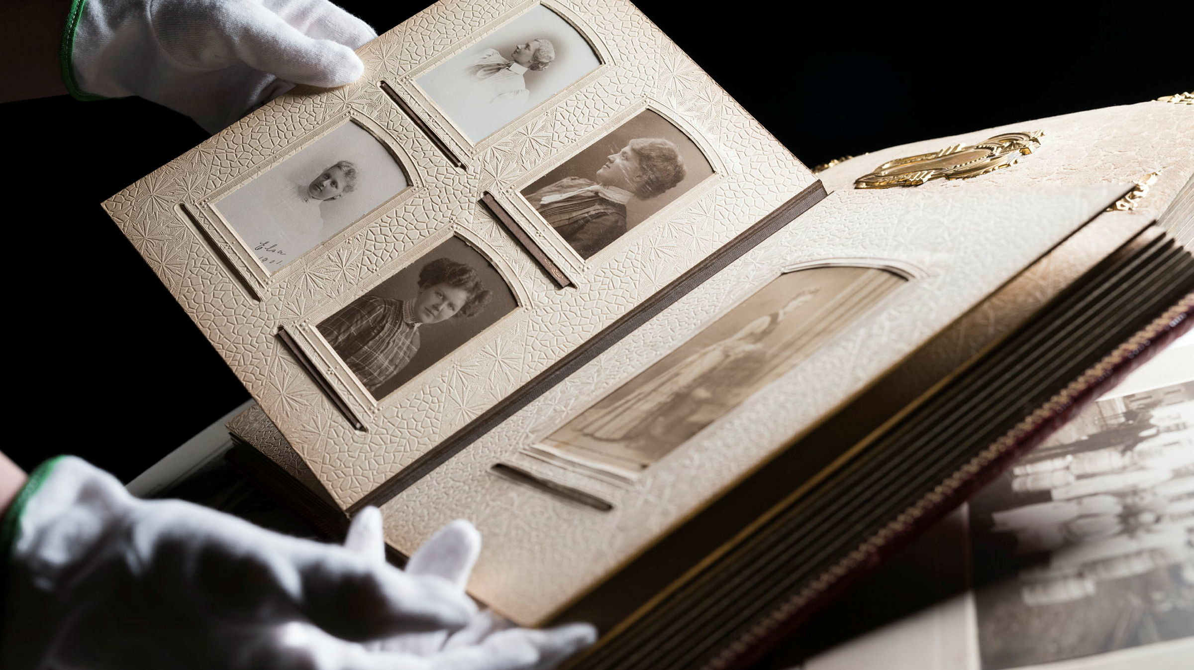 Ett par handskbeklädda händer håller i ett äldre fotoalbum.