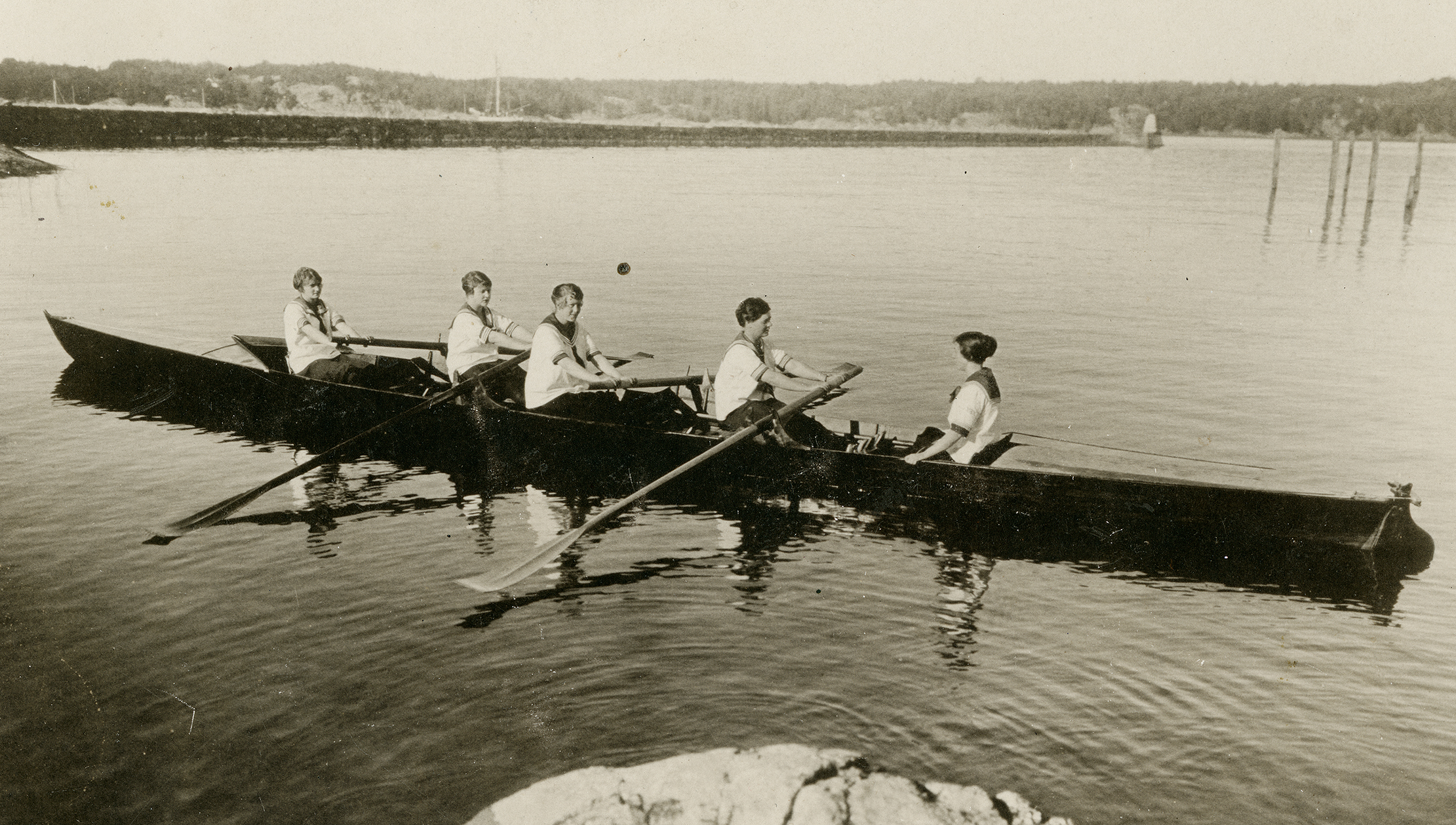 Fem roddare i en roddbåt.