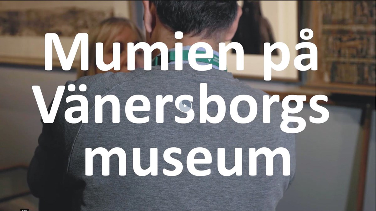 En mans rygg framför en kvinna. Text Mumien på Vänersborgs museum.